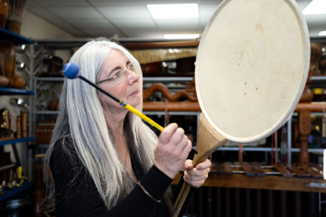 Evelyn stood, striking a Uchiwa Daiko, also known as a Pancake Drum or Fan Drum, from The Evelyn Glennie Collection.